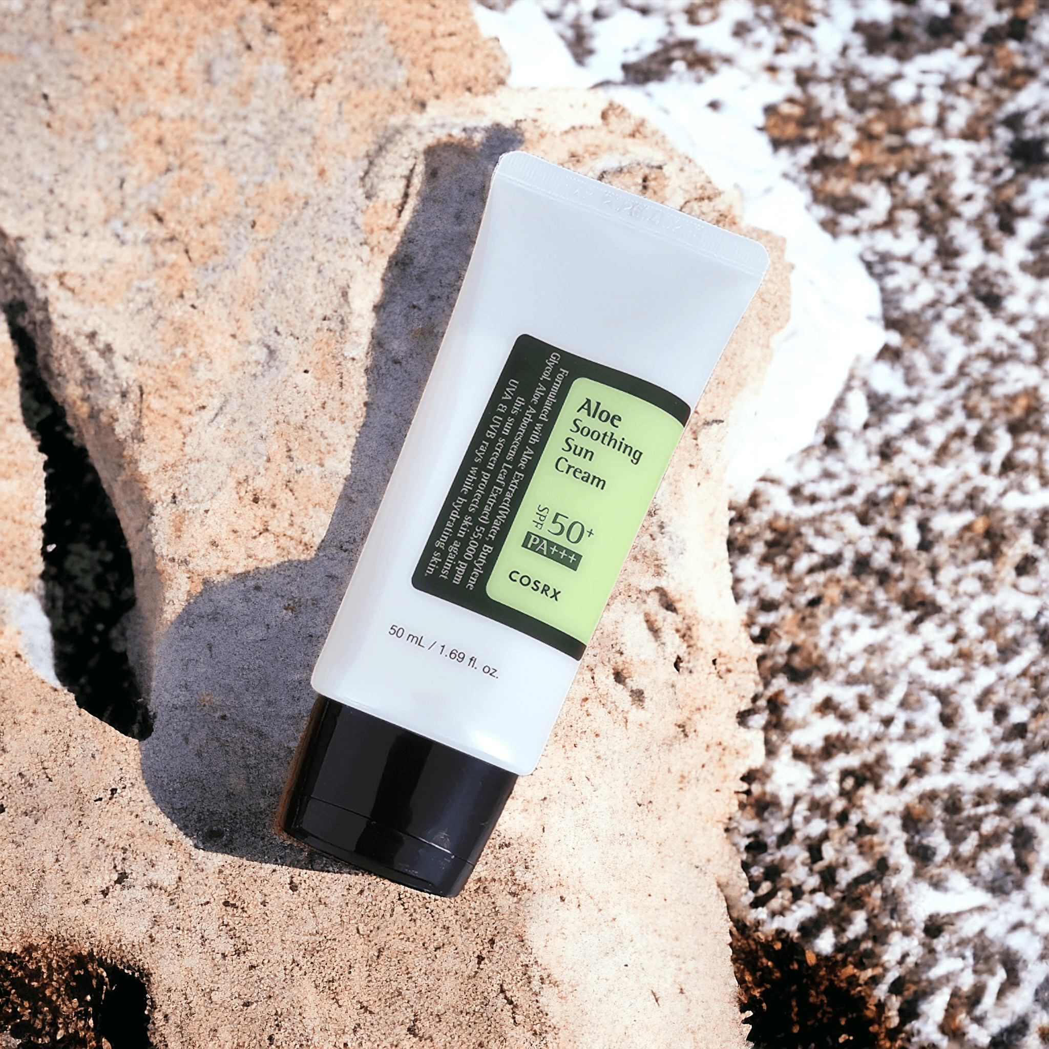 COSRX - Aloe Soothing Sun Cream with shadow lying down with a coastal background 