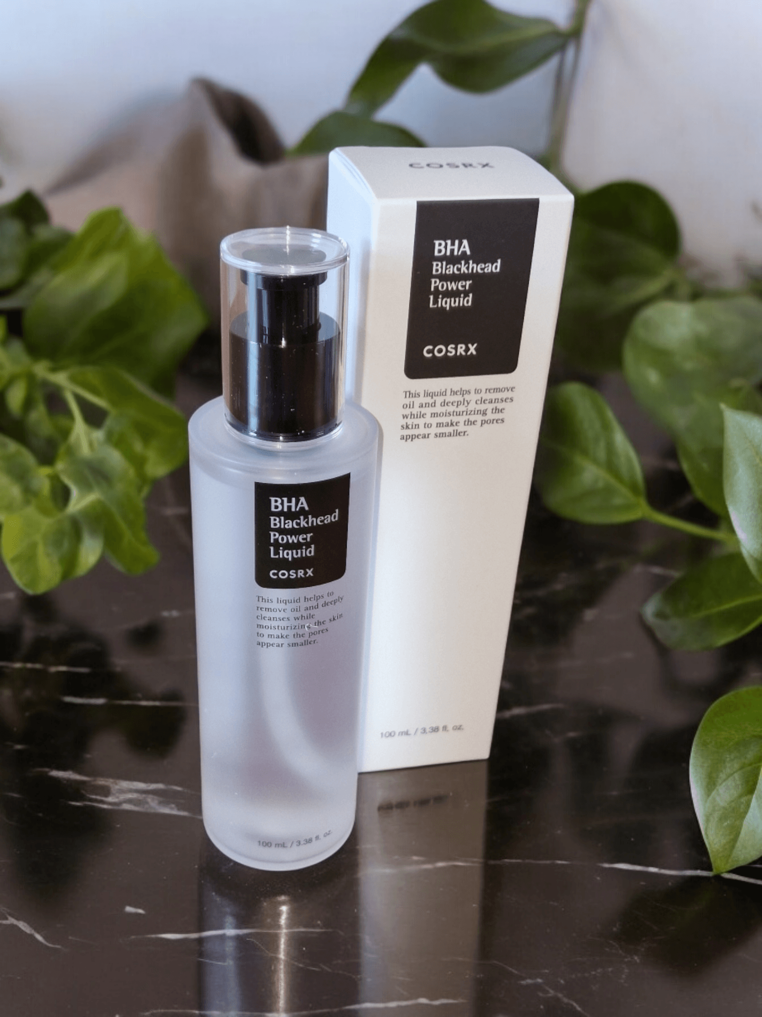 COSRX - BHA Blackhead Power Liquid next to box on a black counter surrounded by plants